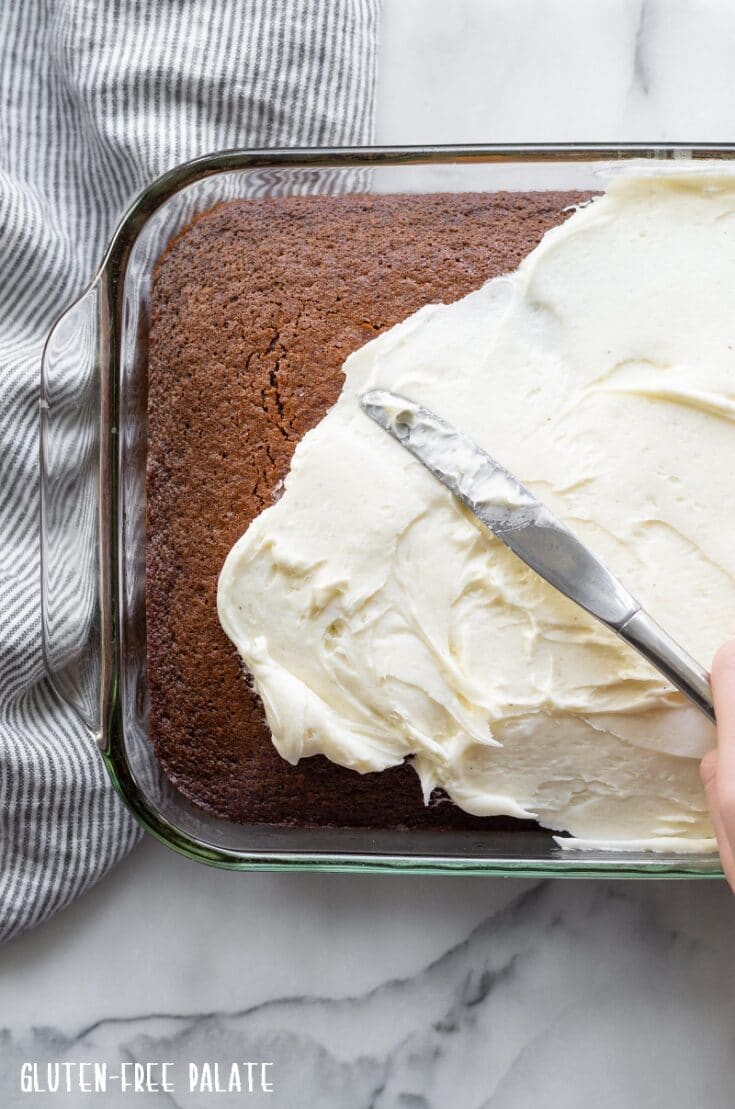 a knife frosting a gluten free gingerbread cake with white frosting