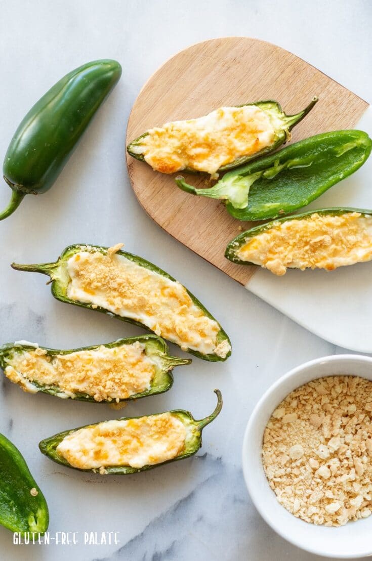 jalapeno poppers on a cutting board with a white bowl of crackers crumbs next to it
