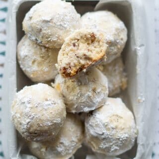 gluten free snow ball cookies in a square metal tin lined with wax paper, one cookie has a bite out