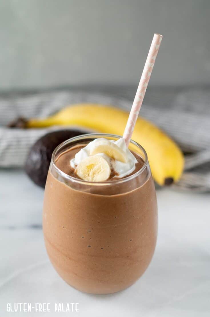 Chocolate Avocado Smoothie in a glass with a pink straw and whipped cream and a sliced banana on top
