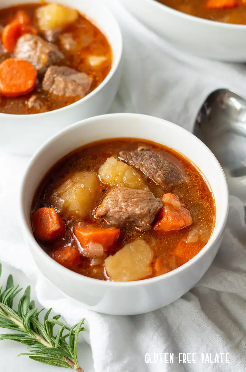side veiw of two bowls of gluten-free beef stew in a white bowl with beef, carrots, and pototoes