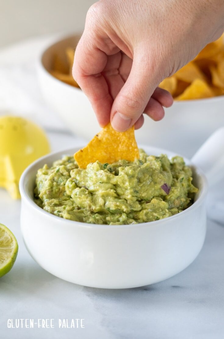 a yellow chip dipping into guacamole in a white bowl