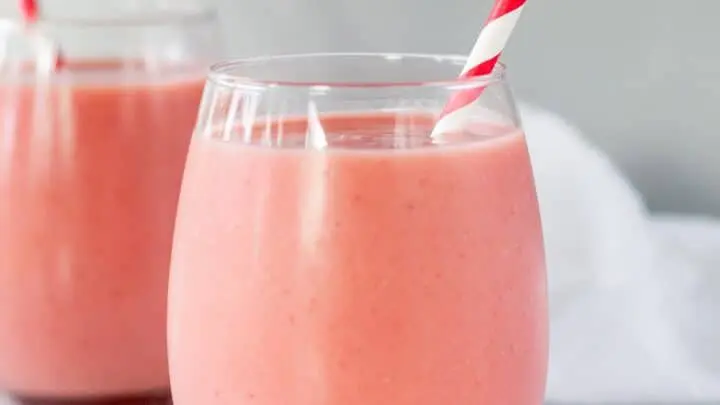 close up of a clear glass with pin strawberry pinapple smoothie and a red and white striped straw