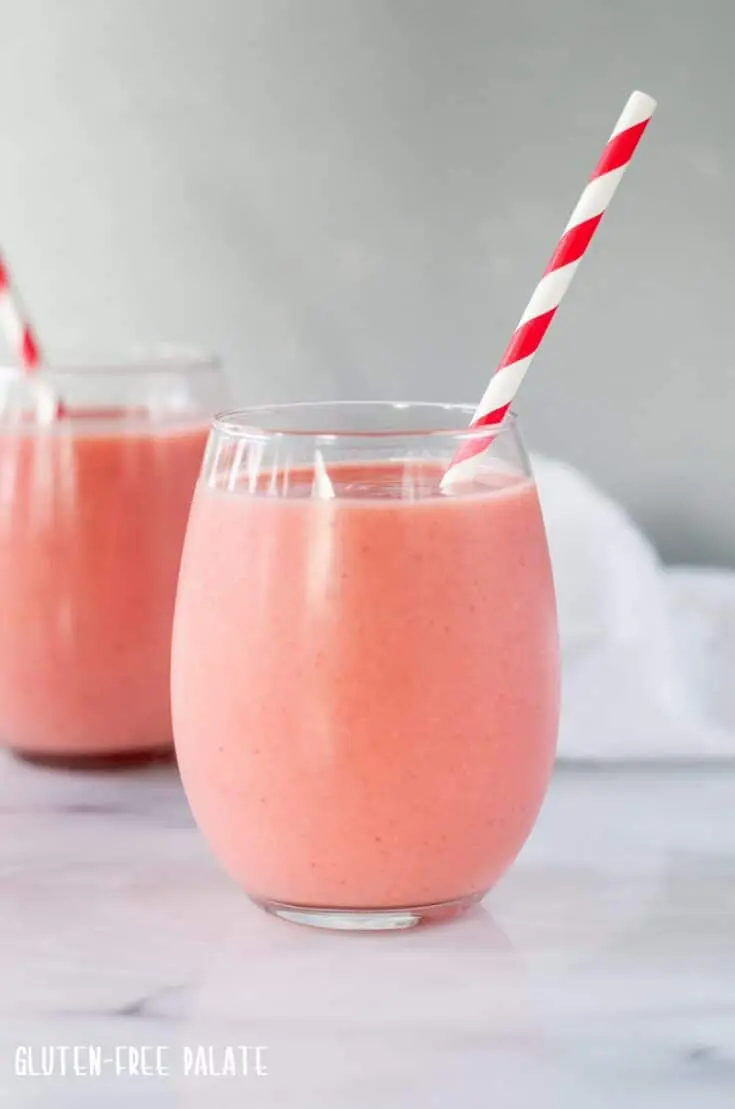 strawberry pineapple smoothie in a clear glass with a red and white stripe straw