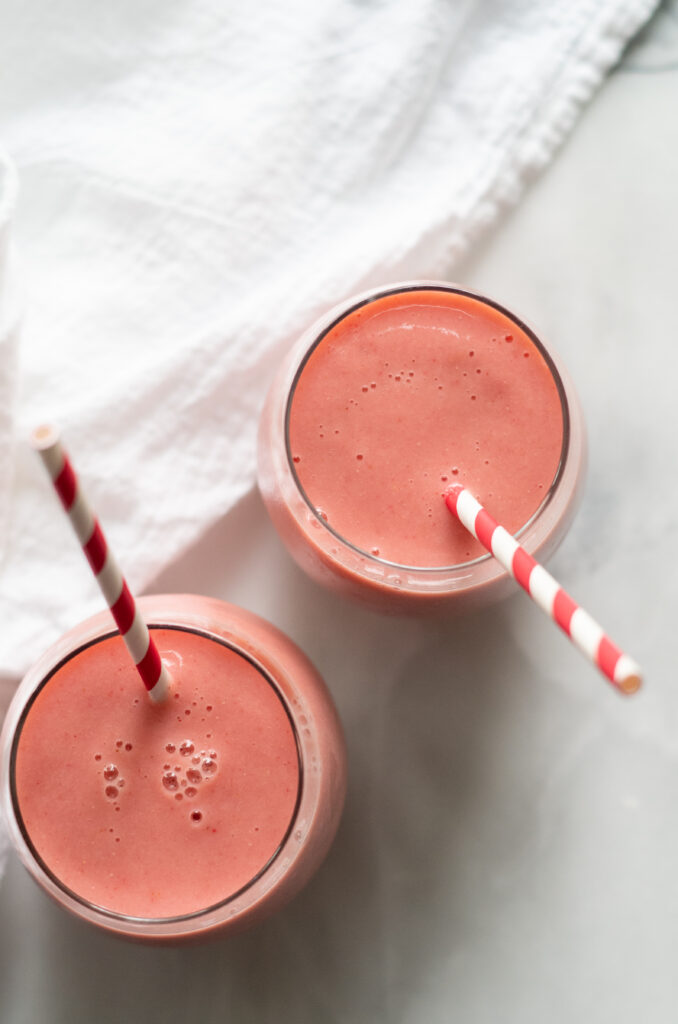 Two strawberry pineapple smoothies with straws.