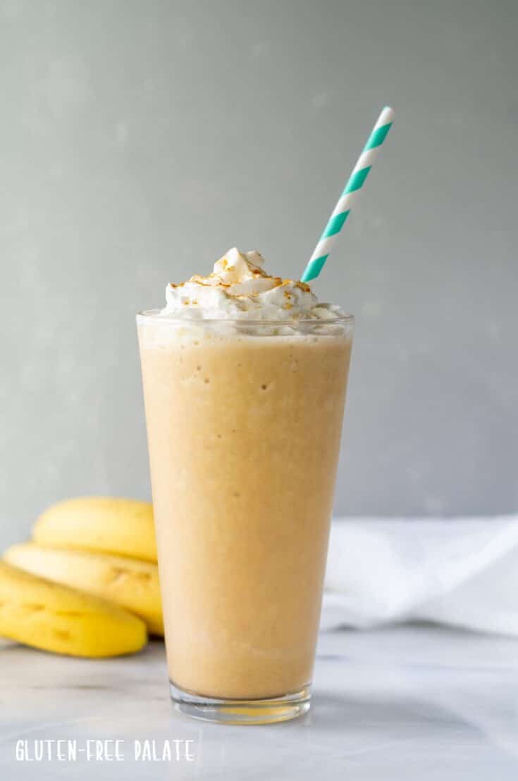 Turmeric Smoothie in a tall clear glass with a straw, topped with whipped cream and turmeric