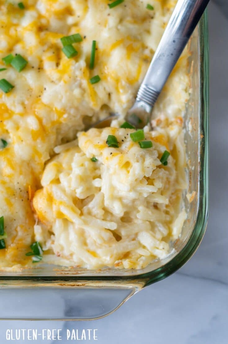 close up of a large spoon dipping into cheesy potatoes in a glass baking dish