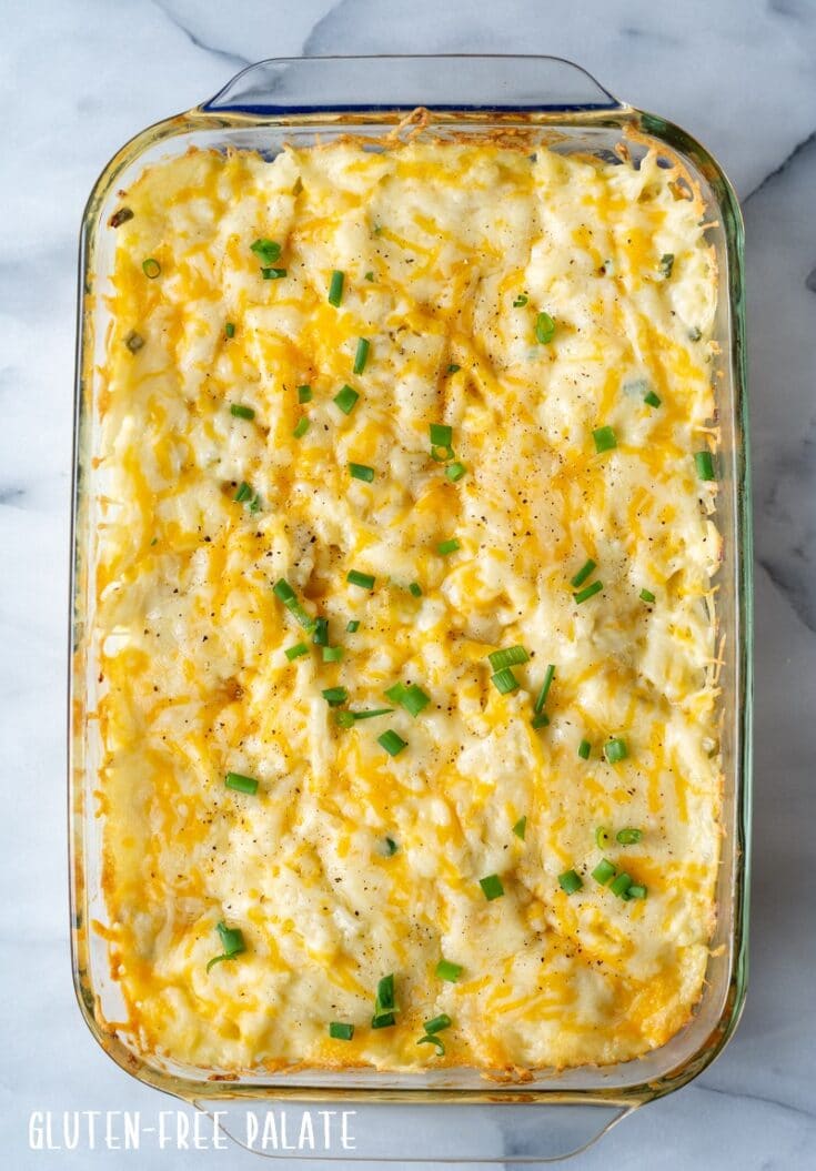 Cheesy Potatoes in a glass baking pan on a marble background with chopped green onions on top