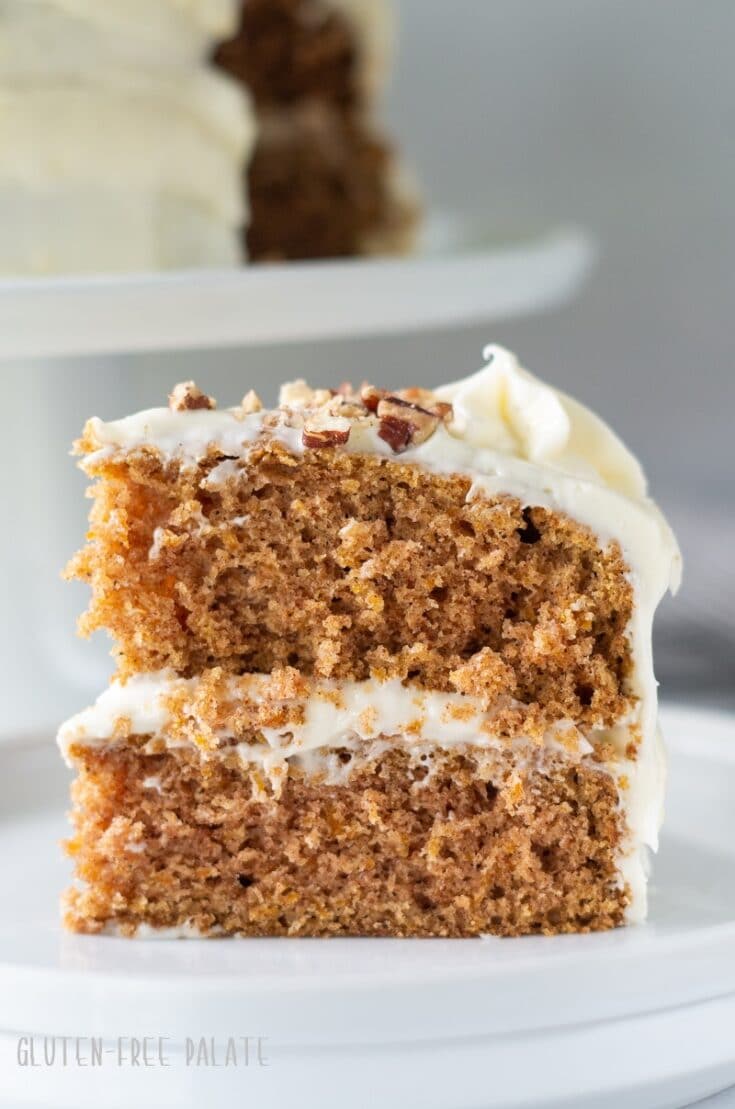 close up of a slice of gluten free carrot cake topped with frosting and chopped nuts on a white plate
