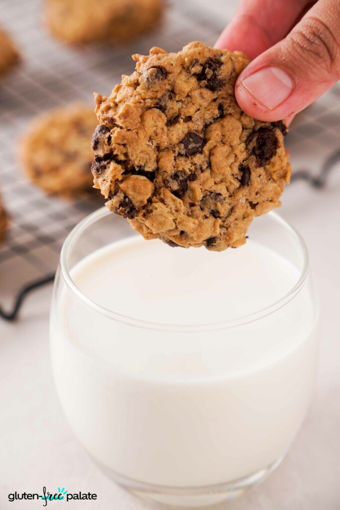 Close up of Gluten-Free oatmeal cookies being held in a hand above a glass of milk.