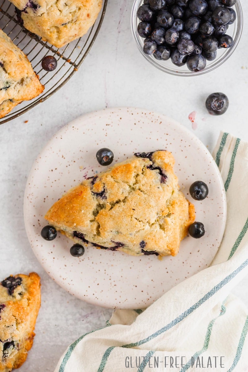 a gluten-free blueberry scones on a white textured plate with blueberries and a towel