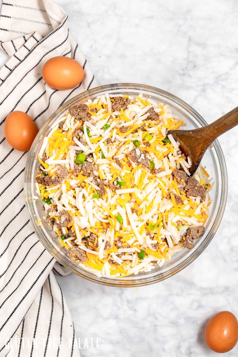 a bowl filled with sausage, cheese, hashbrowns, and green onion to make gluten-free breakfast casserole