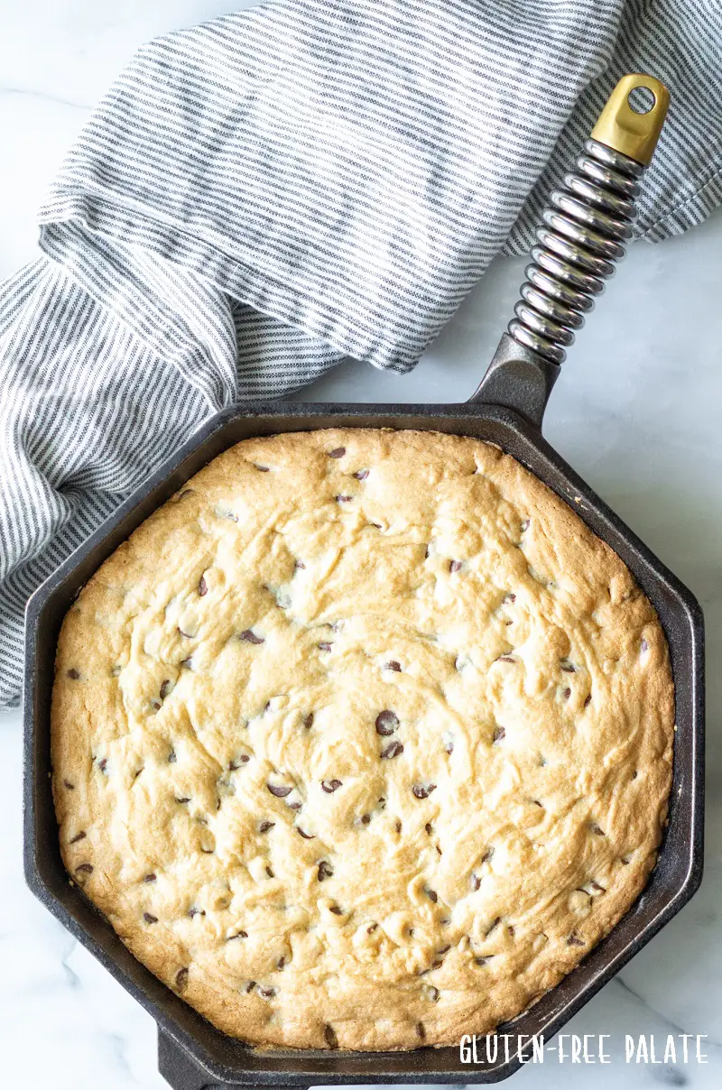 a gluten free chocolate chip skillet cookie in a cast iron skillet next to a stripe napkin