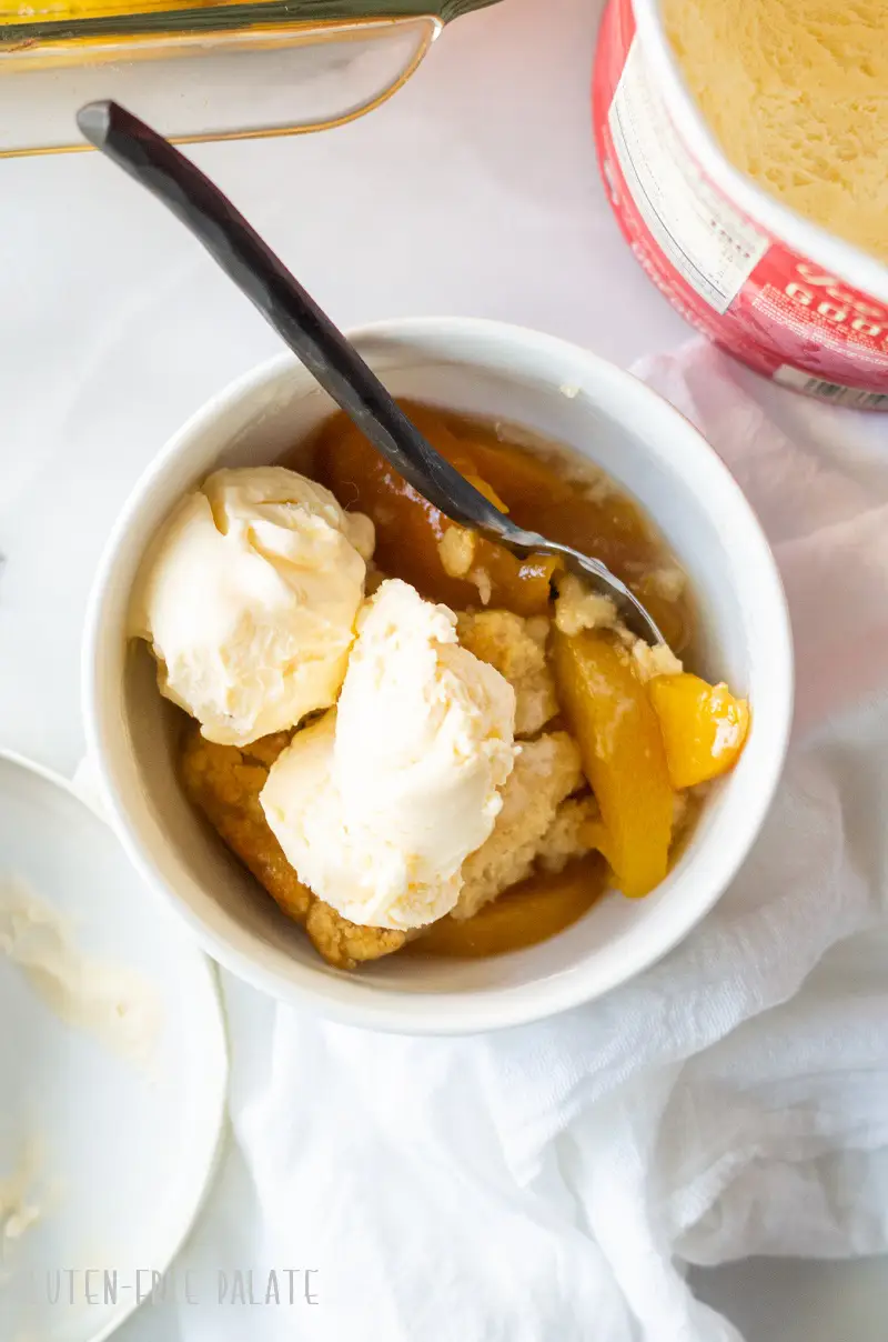 gluten-free peach cobbler in a white bowl topped with two scoops of vanilla ice cream