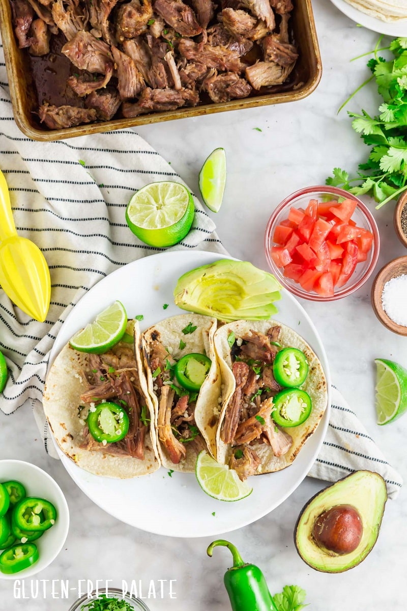 shredded carnitas tacos on a white plate with lime wedges and avocado slices