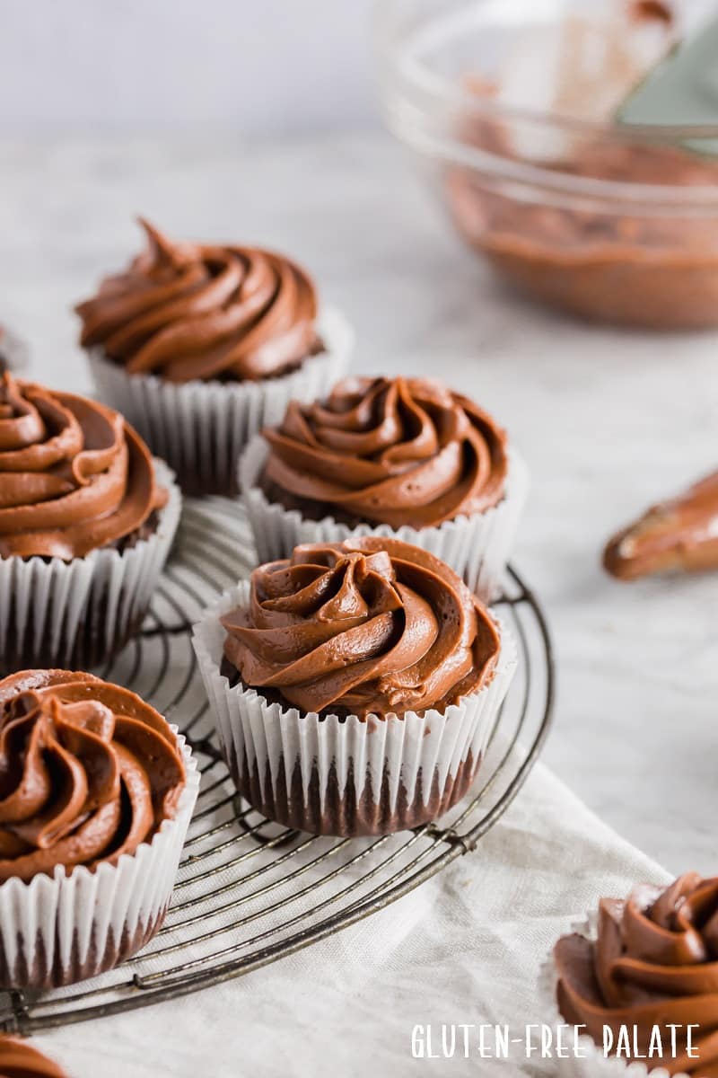 chocolate cupcakes in white paper liners topped with chocolate frosting, on a wire cooling rack