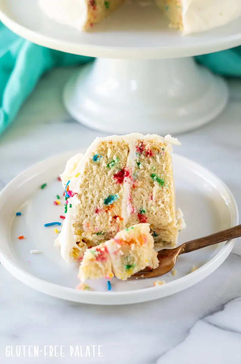 a slice of gluten free funfetti cake on a white plate with a gold fork