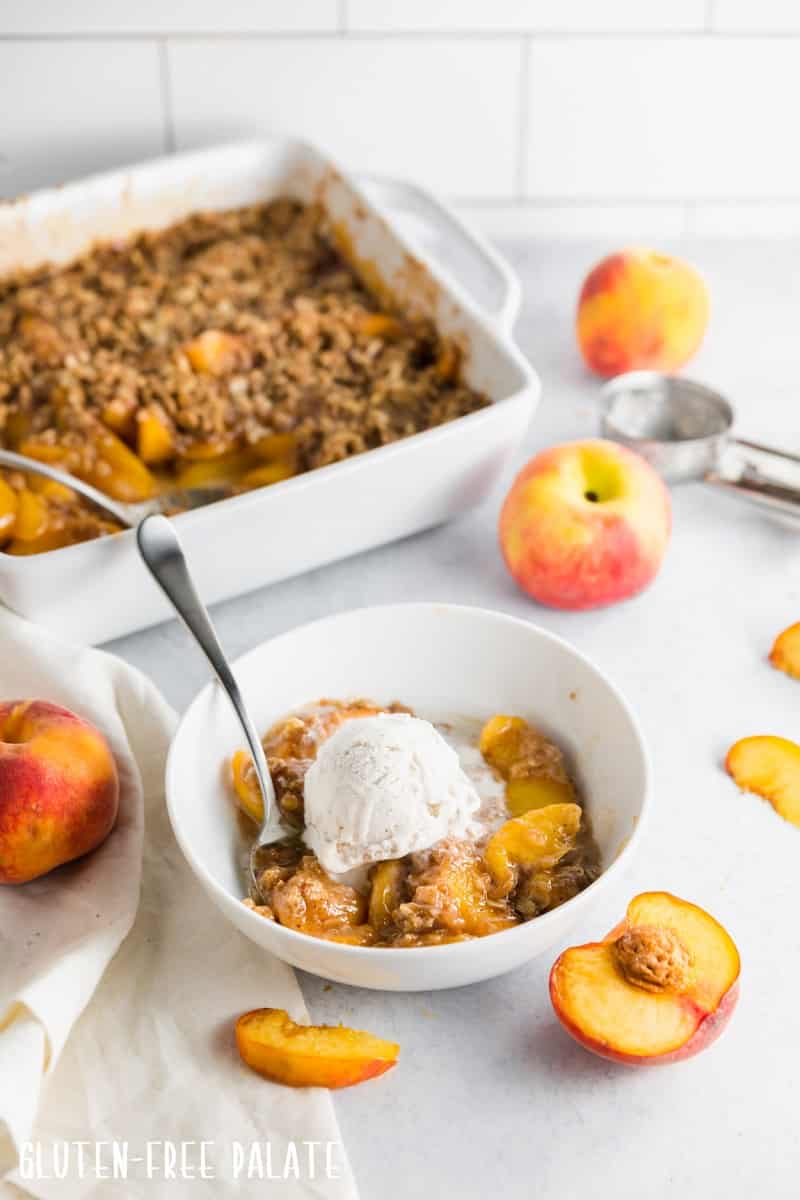 gluten free peach crisp in a white bowl topped with ice cream