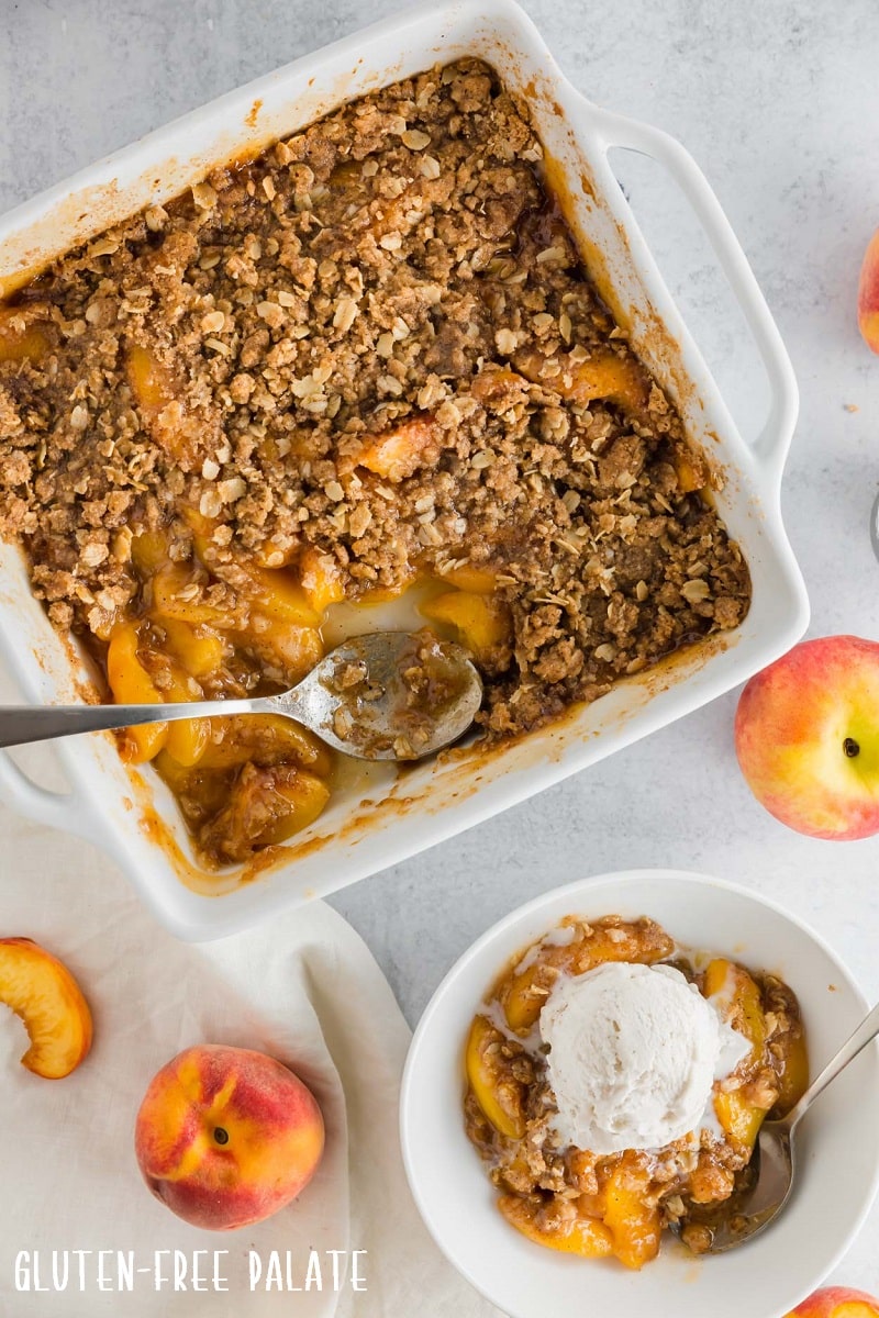top down view of gluten-free peach crisp in a white baking pan next to a bowl of crisp topped with vanilla ice cream