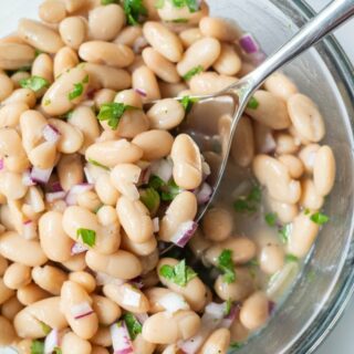 a spoon serving a scoop of white bean salad from a clear bowl