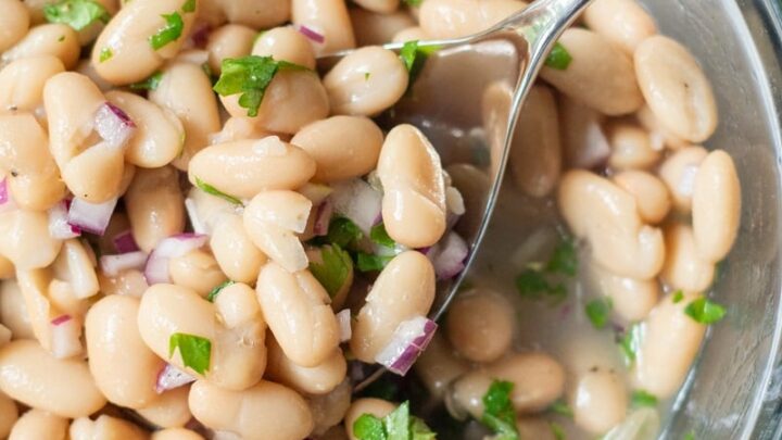 a spoon serving a scoop of white bean salad from a clear bowl