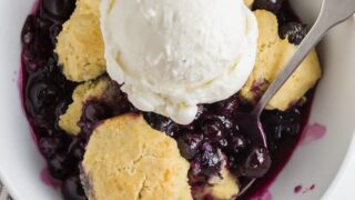 a close up of gluten free blueberry cobbler topped with a scoop of vanilla ice cream