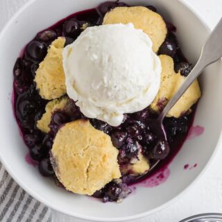 a close up of gluten-free blueberry cobbler topped with a scoop of vanilla ice cream