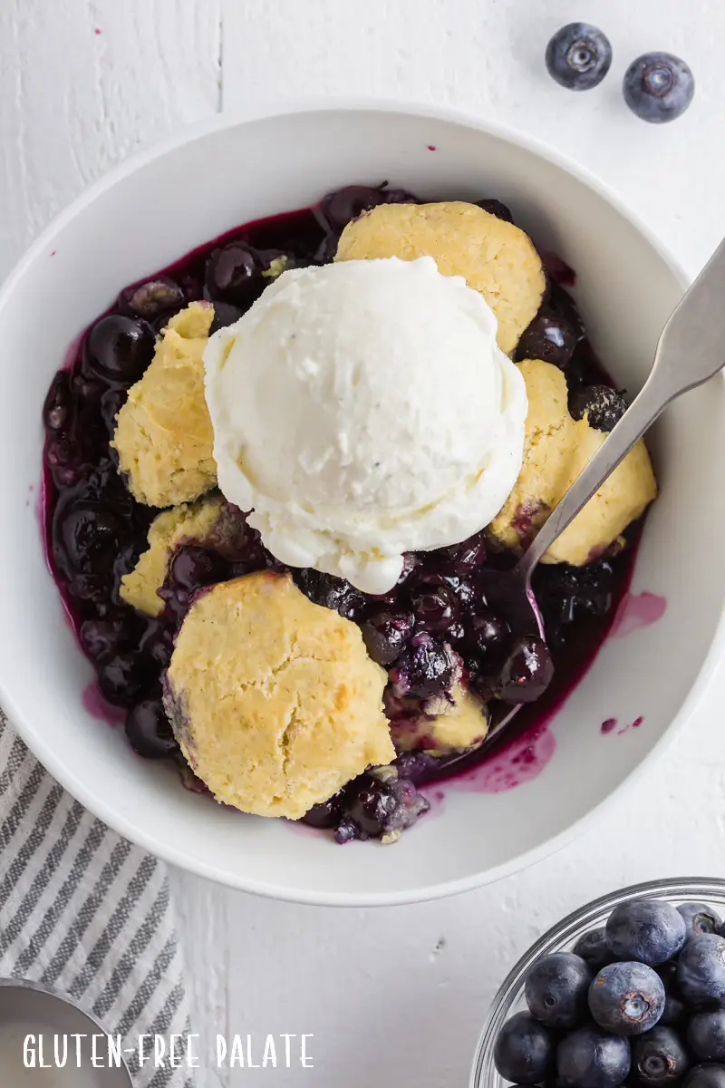 a close up of gluten-free blueberry cobbler topped with a scoop of vanilla ice cream