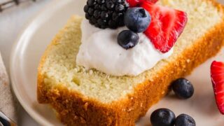 a close up of a slice of gluten free pound cake topped with whipped cream and berries