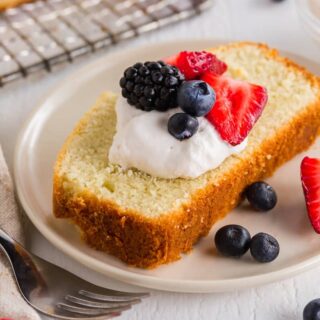 a close up of a slice of gluten-free pound cake topped with whipped cream and berries