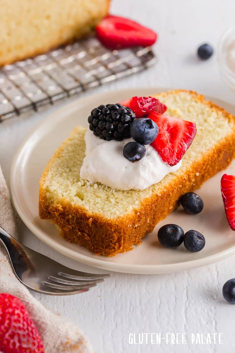 a close up of a slice of gluten free pound cake topped with whipped cream and berries
