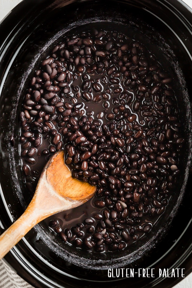 top down view of black beans in a crockpot with a wooden spoon
