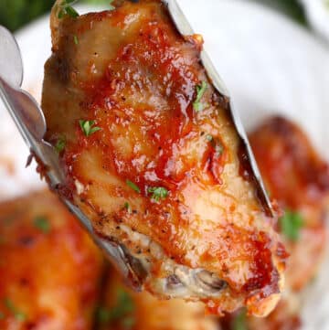 Tongs holding a gluten free chicken wing.
