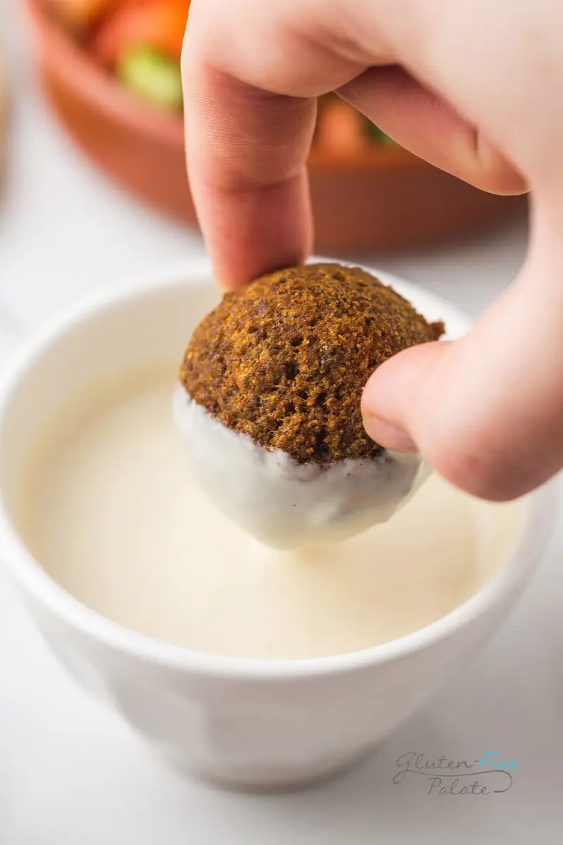 hand dipping a gluten-free falafel into tahini sauce