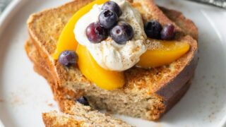 2 slices of gluten free french toast topped with peaches, blueberries, and whipped cream
