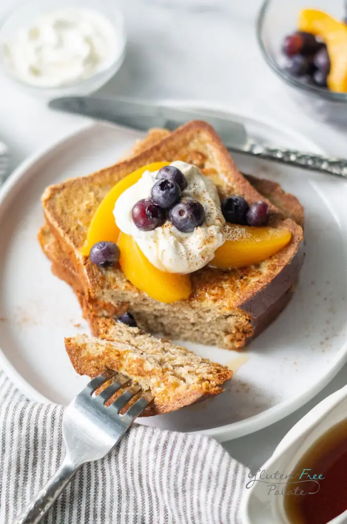 2 slices of gluten-free French toast topped with peaches, blueberries, and whipped cream.