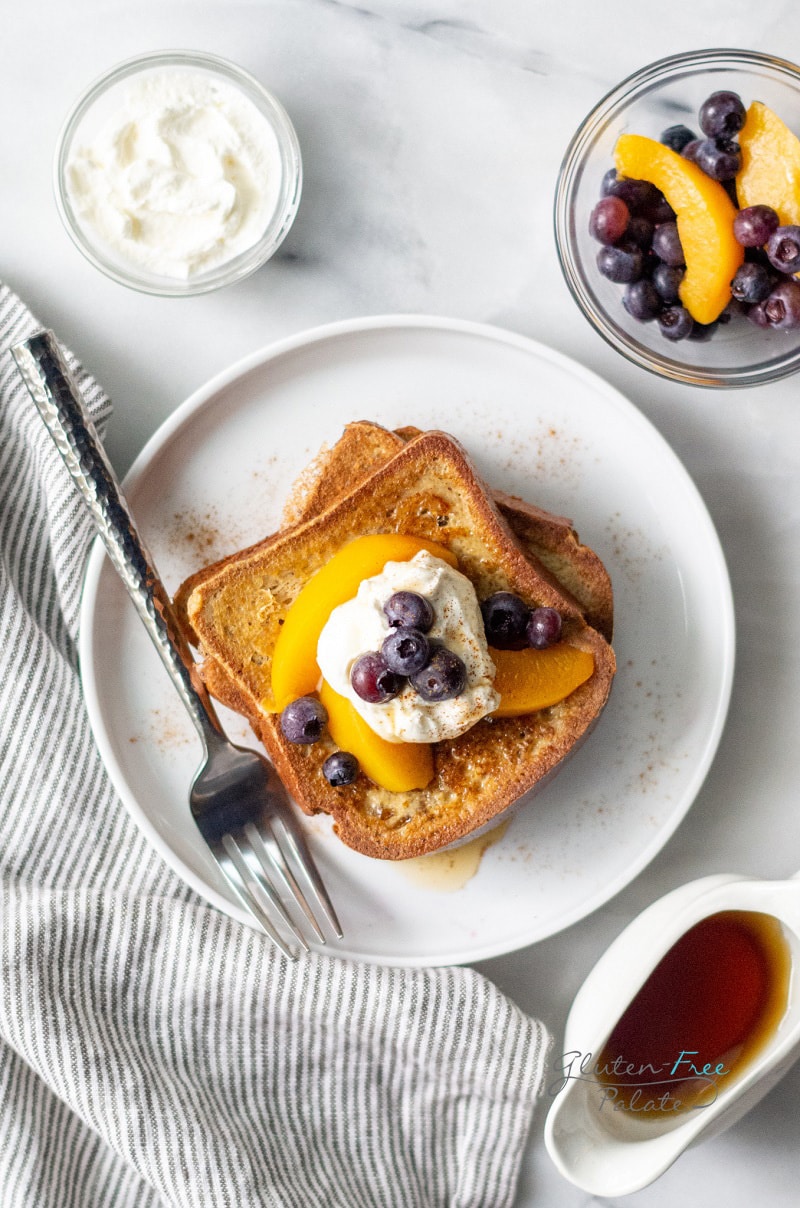 top down view of 2 slices of gluten-free French toast topped with peaches, blueberries, and whipped cream