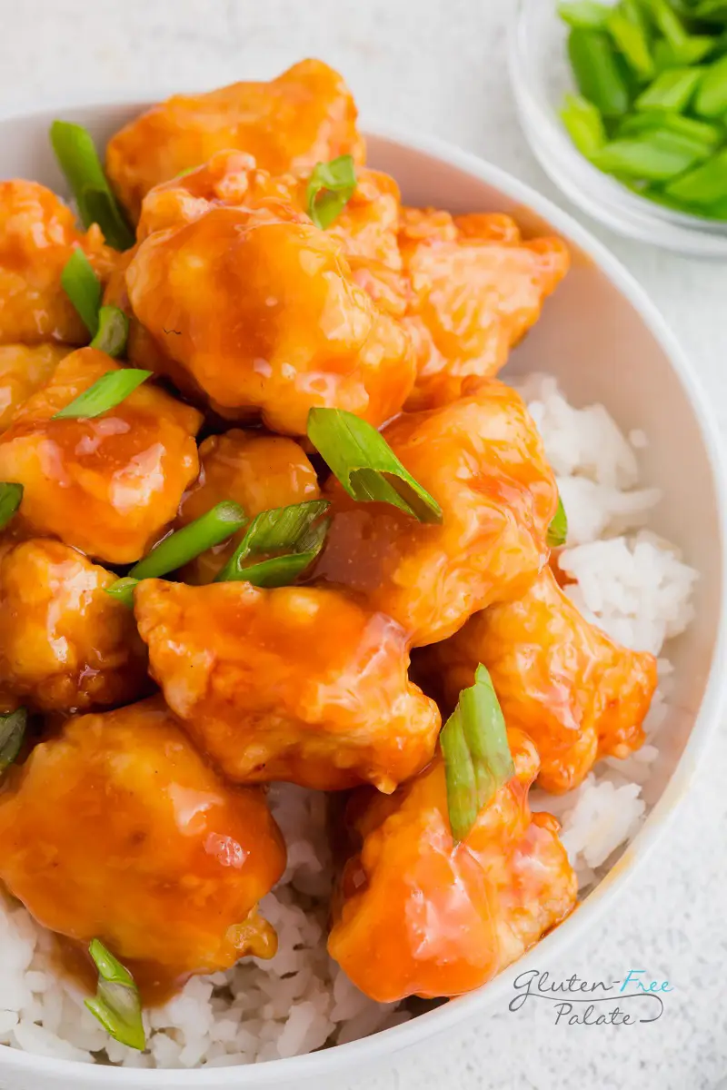 a close up of gluten-free orange chicken over rice in a white bowl