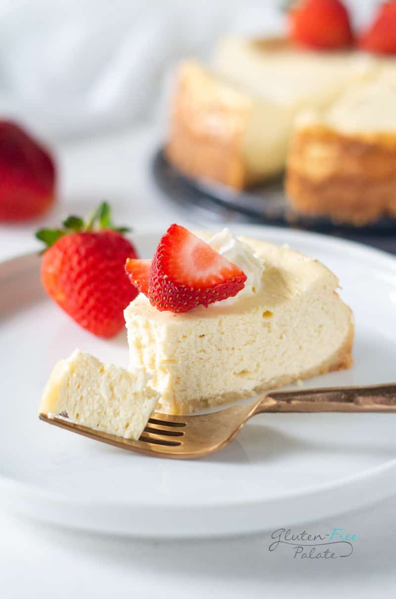 a slice of gluten free cheesecake on a white plate with a bite out and a fork