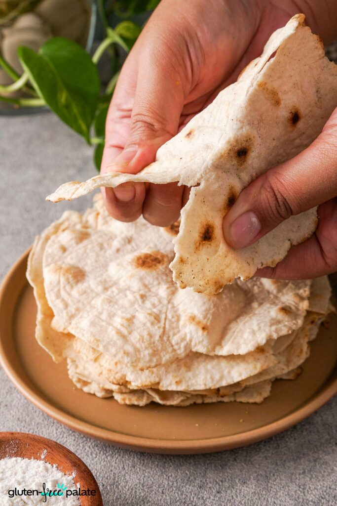 a stack of gluten-free tortillas on a white plate with one being torn to show texture.