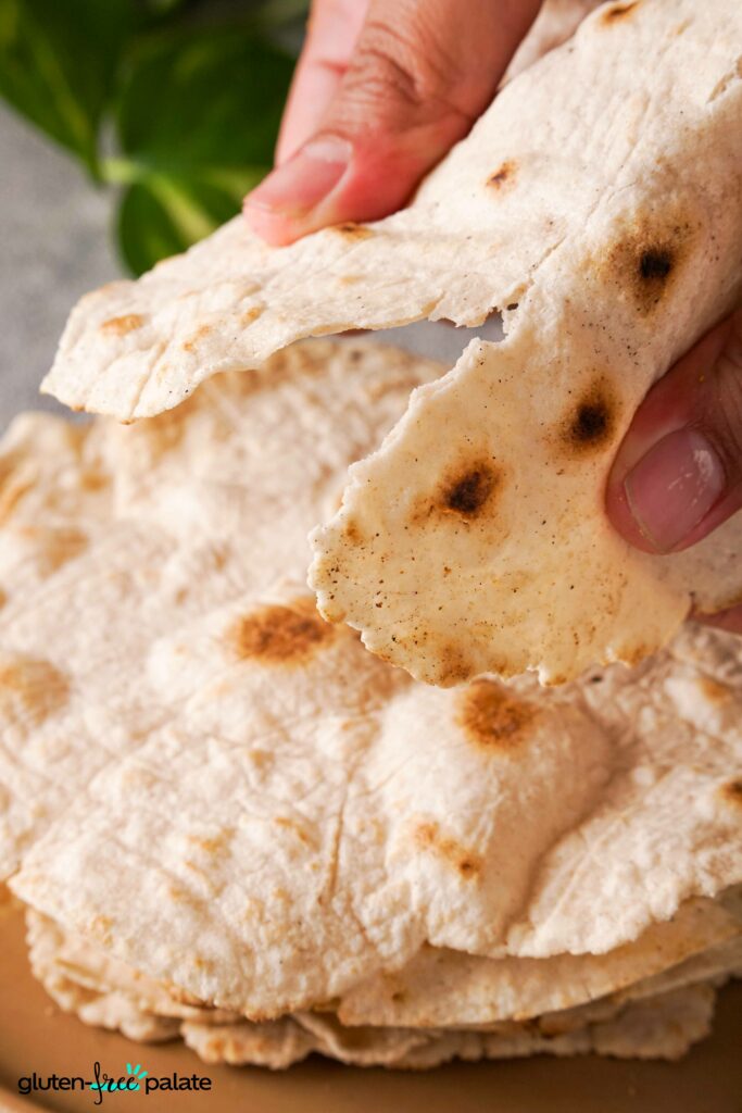 a stack of gluten-free tortillas on a white plate with one being torn to show texture.