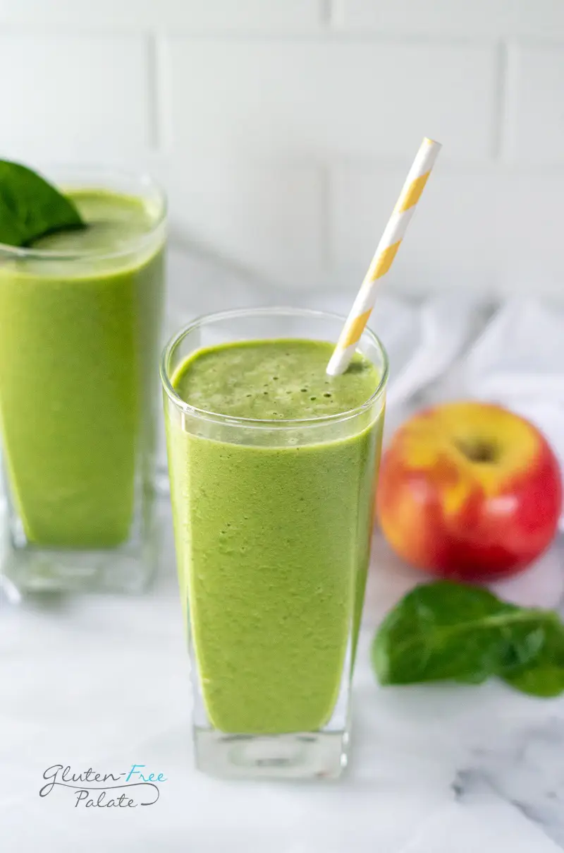 apple spinach smoothie in a glass with a yellow striped straw