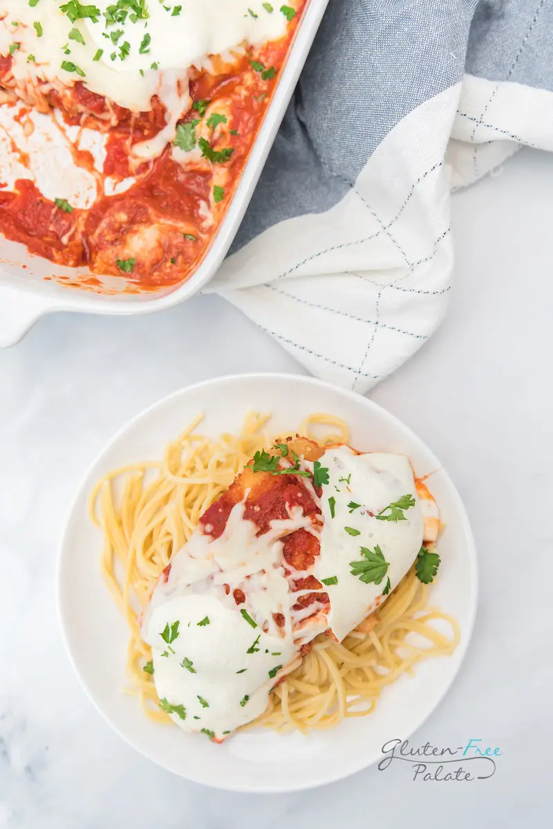 a plate of spaghetti topped with cheesy chicken parmesan, next to a casserole dish of chicken parmesan