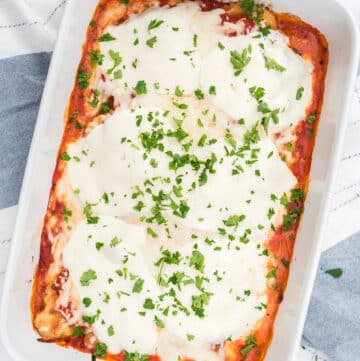 a rectangular casserole dish filled with gluten-free chicken parmesan, topped with cheese and fresh parsley