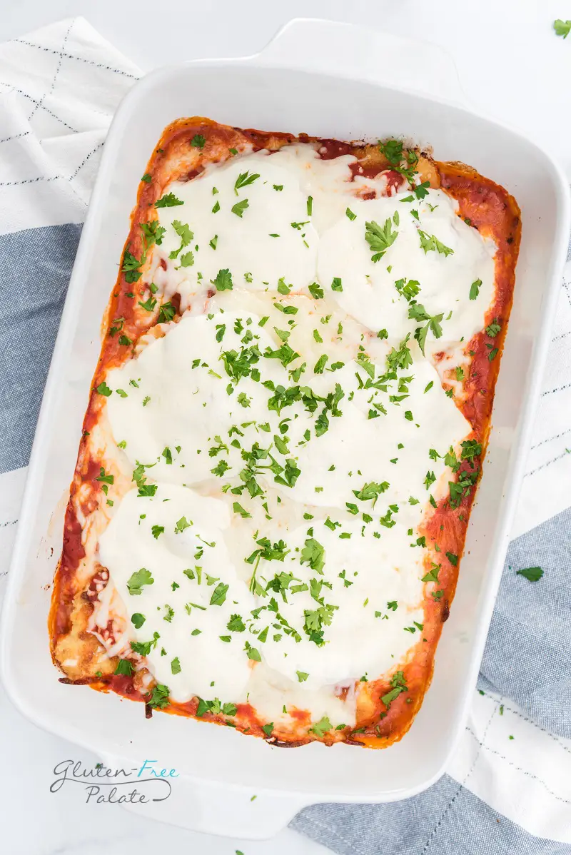 a rectangular casserole dish filled with gluten-free chicken parmesan, topped with cheese and fresh parsley