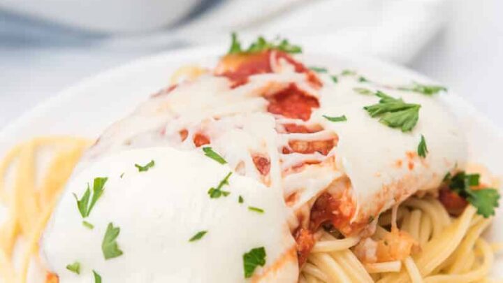 a plate of spaghetti topped with cheesy chicken parmesan.