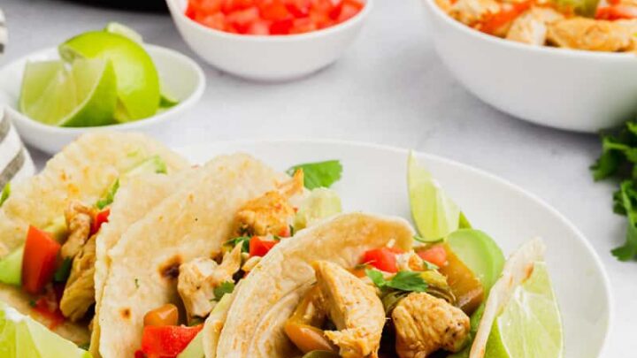 a plate of three soft chicken tacos filled with chicken and peppers, garnished with lime. The plate s in front of an instant pot.