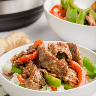 sliced steak with red and green peppers on top of a bowl of rice next to an instant pot