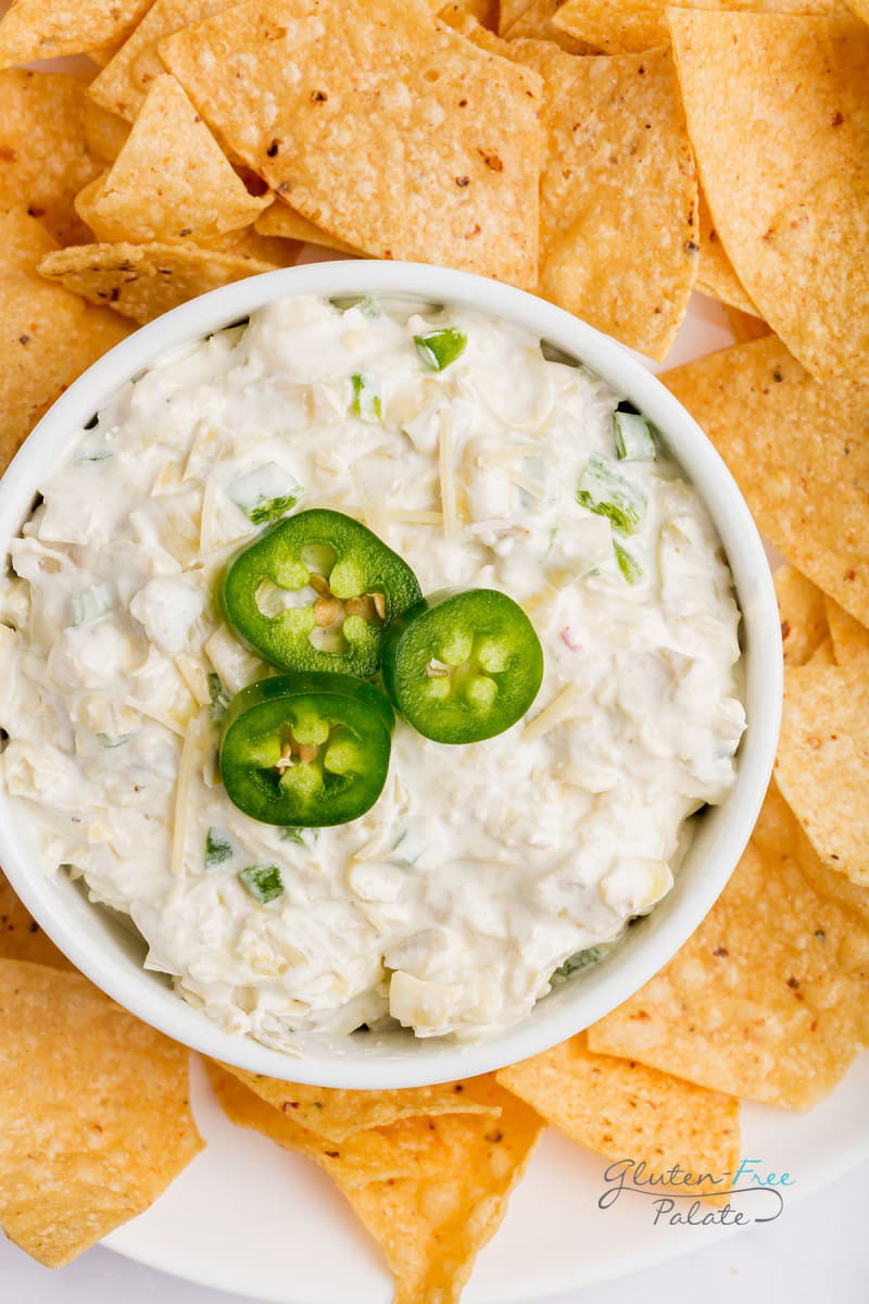 top down view of a bowl of dip with three jalapeno slices on top, surrounded by tortilla chips.