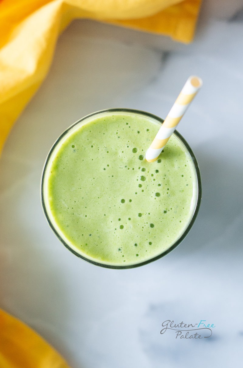 top down view of a pineapple spinach smoothie in a glass with a straw